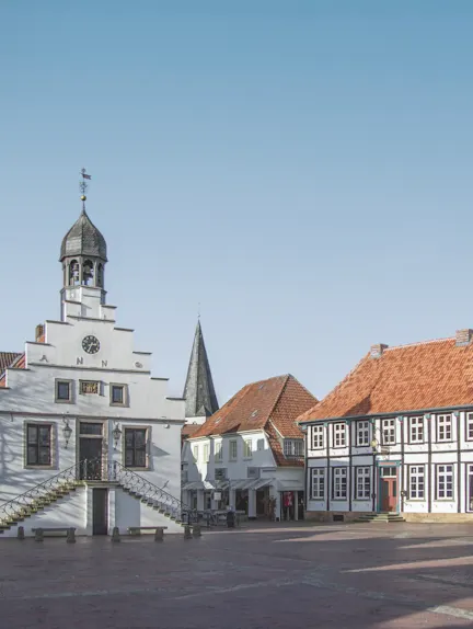Historische Gebäude mit roten Dächern und einem weißen Turm an einem sonnigen Platz.
