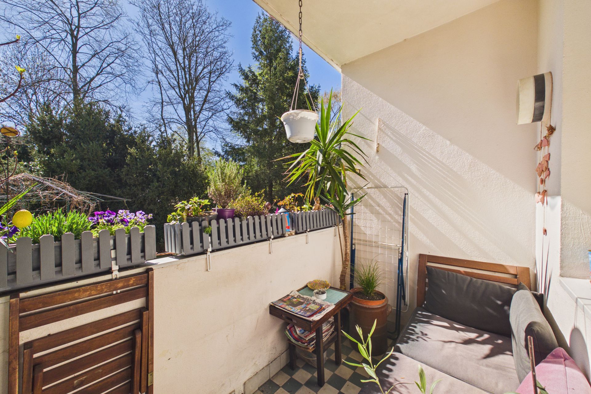 Kleiner Balkon mit Blumenkästen, Sitzbank, Tisch und Pflanzen bei Tageslicht.