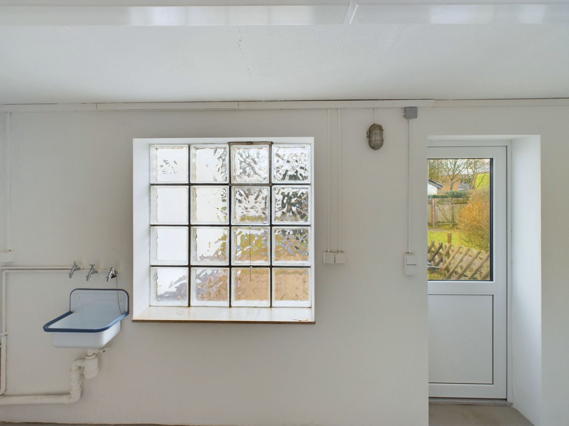 Weißer Raum mit einem Waschbecken, einem Glasbaustein-Fenster und einer Tür nach draußen.