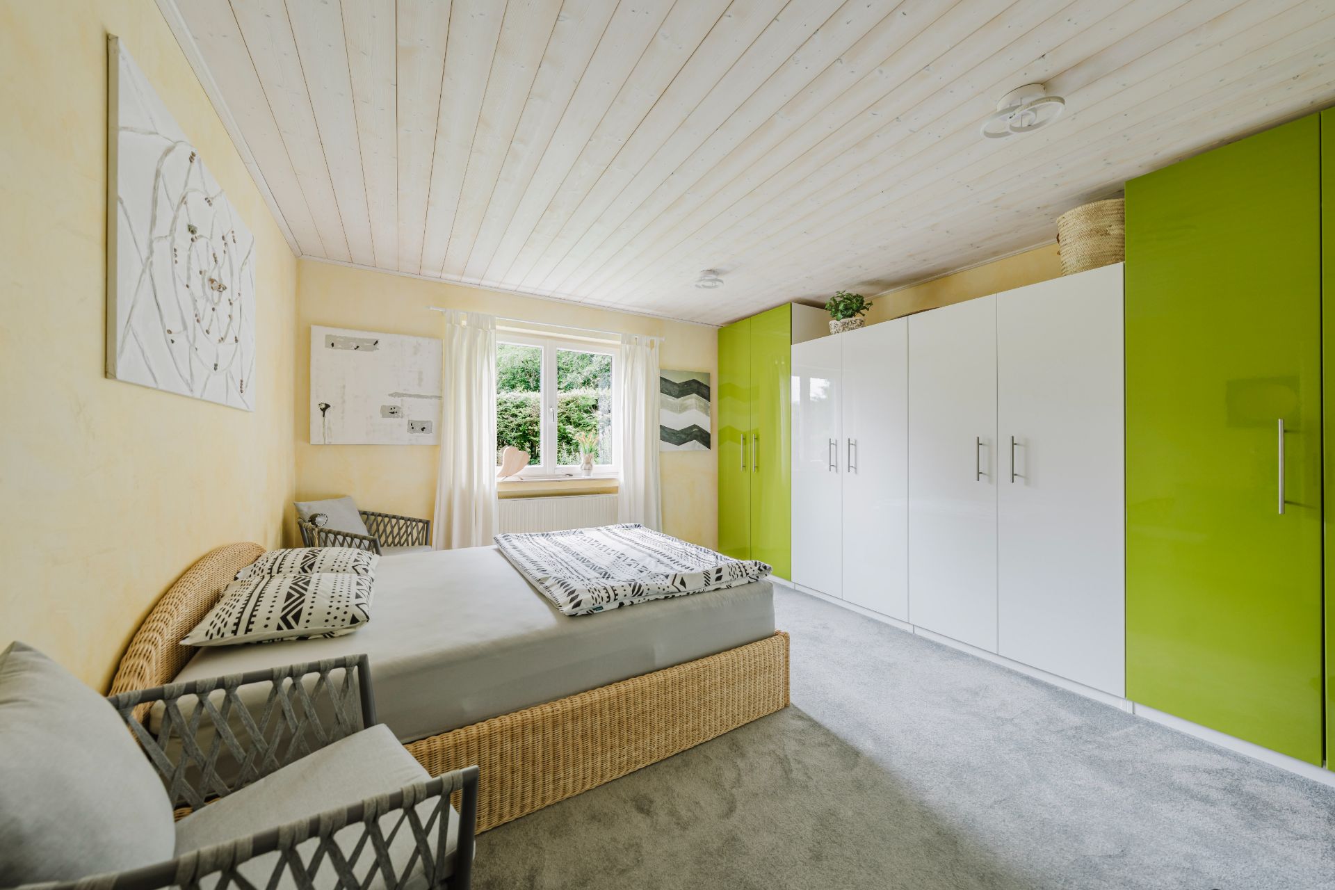 Helles Schlafzimmer mit Bett, Stühlen, großem Kleiderschrank und Fenster mit Blick ins Grüne.
