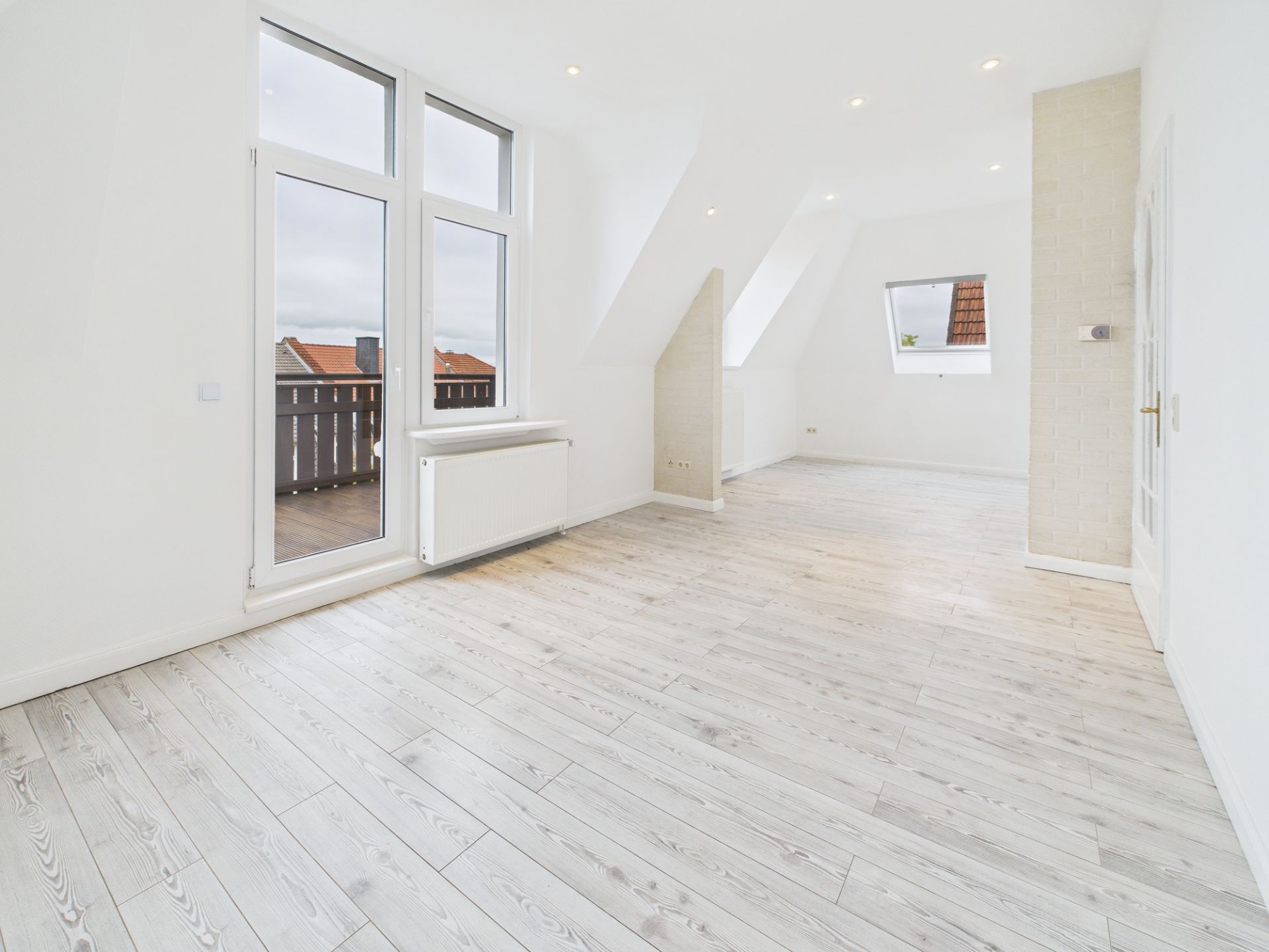 Heller Wohnraum mit Holzfußboden, großen Fenstern und Zugang zu einem Balkon.