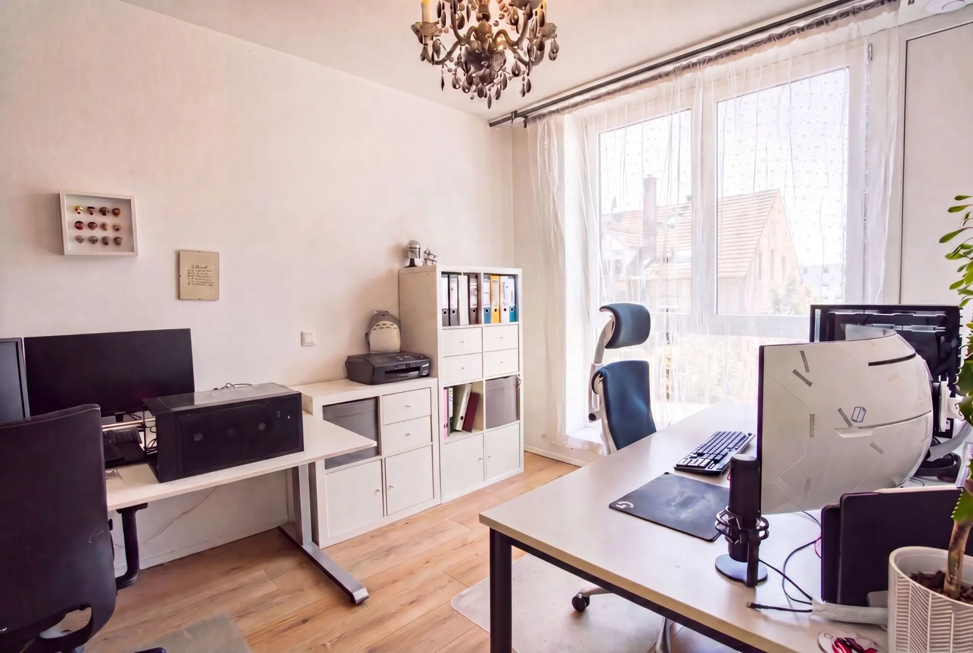 Helles Arbeitszimmer mit zwei Schreibtischen, Monitoren, Regalen und großem Fenster.