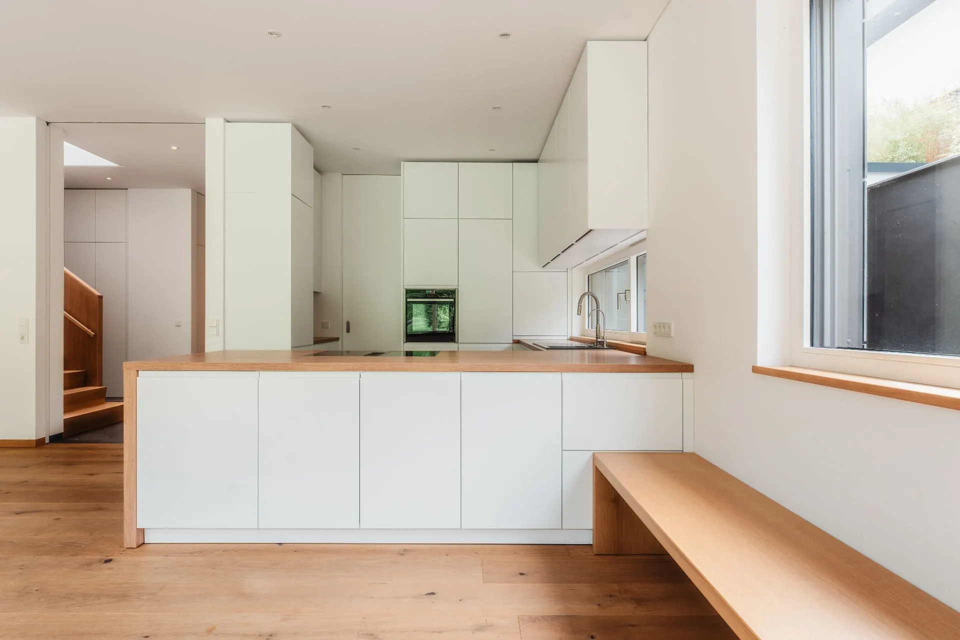 Moderne weiße Küche mit Holzarbeitsplatte, großer Fensterbank und Sitzbank aus Holz.