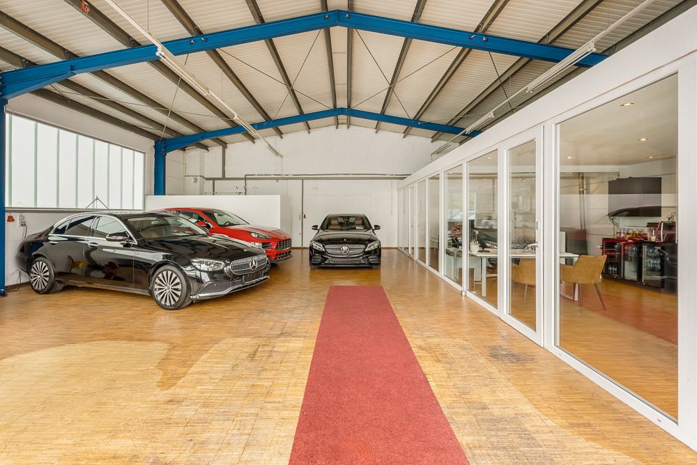 Große Garage mit drei geparkten Autos, rotem Teppich und angrenzendem verglasten Büroraum.