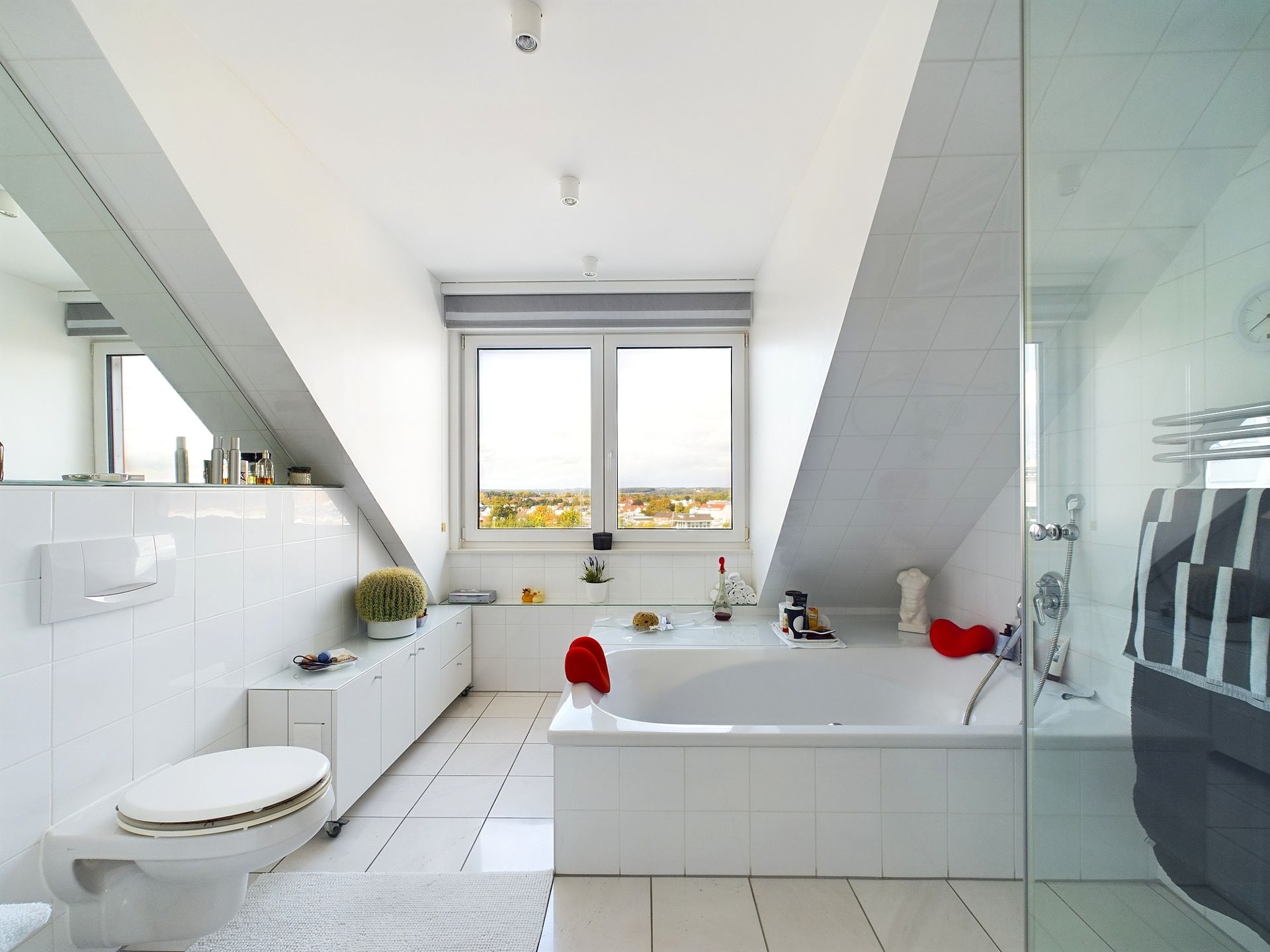 Modernes Badezimmer mit Badewanne, Toilette, Fenster und schräger Decke.