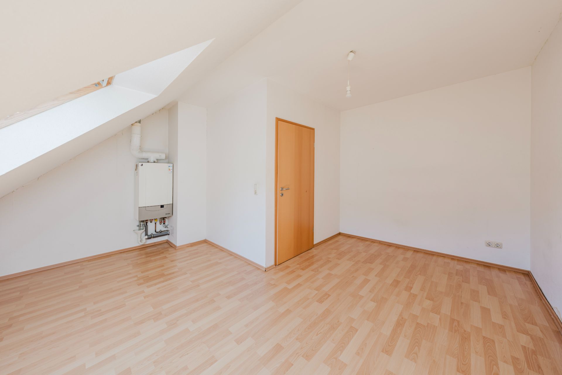 Leeres Zimmer mit Dachschräge, Holzfußboden und Heizungsanlage an der Wand.