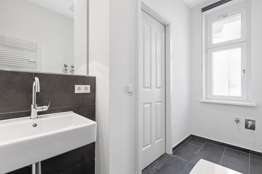Modernes Badezimmer mit Waschbecken, Fenster und grauen Fliesen.