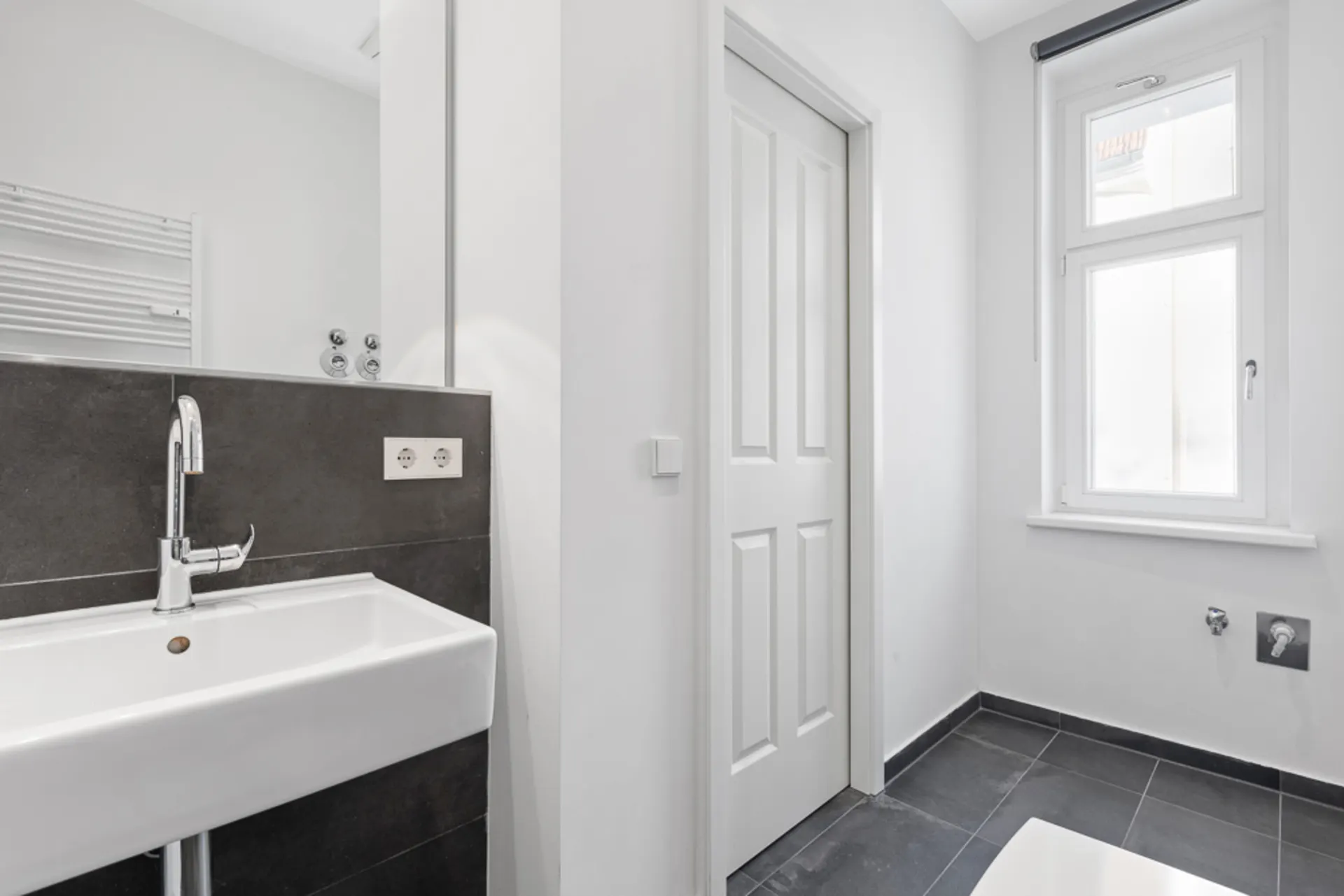 Modernes Badezimmer mit Waschbecken, Fenster und grauen Fliesen.