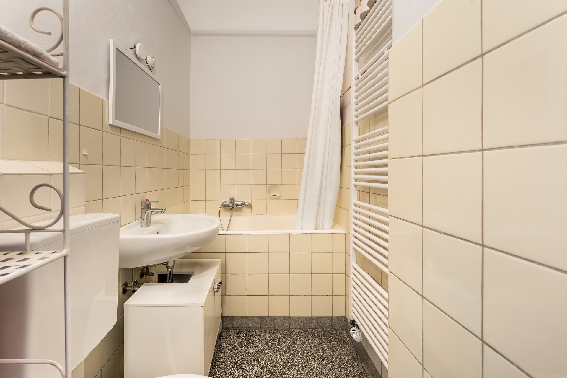 Kleines Badezimmer mit Waschbecken, Toilette, Badewanne, Handtuchheizkörper und helle Fliesen.