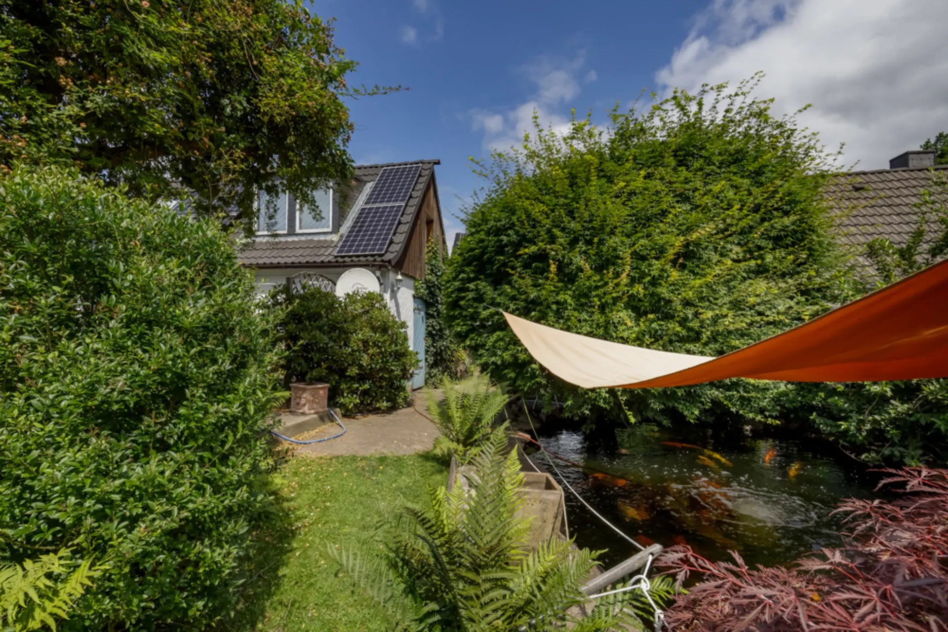 Garten mit kleinem Teich, Sonnensegel und Haus mit Solarpanel auf dem Dach.