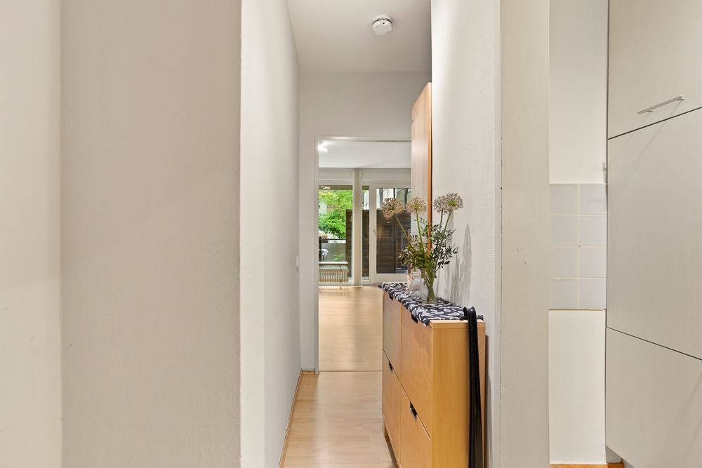 Heller Flur mit Holzkommode und Blumen, Blick ins Wohnzimmer mit großen Fenstern.