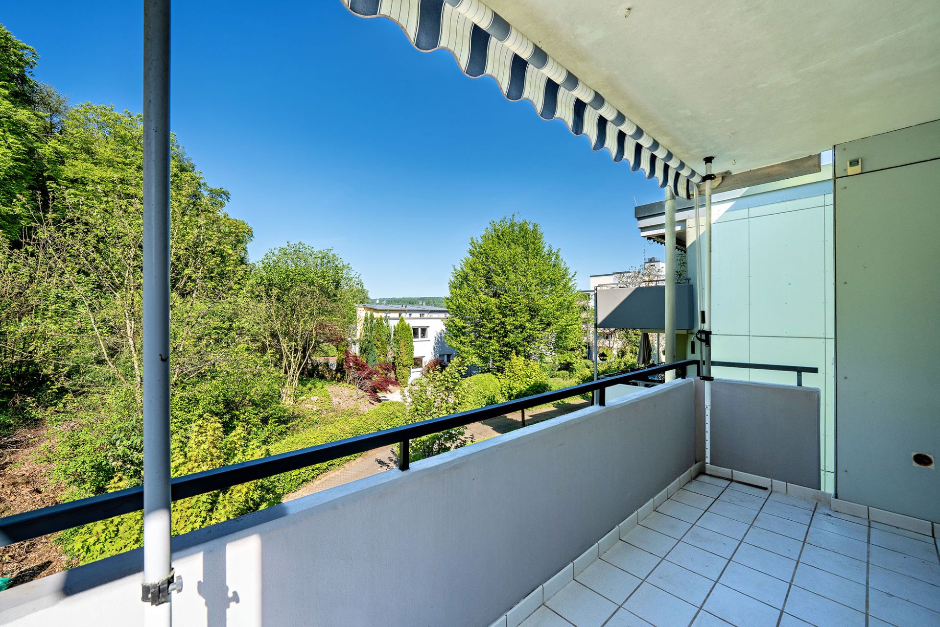 Balkon mit Markise und Blick auf Garten und Bäume an einem sonnigen Tag.