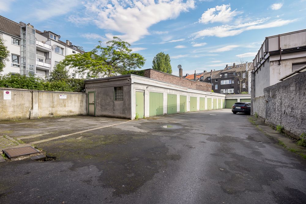 Mehrere Garagen mit grünen Toren und ein geparktes Auto in einem Innenhof.