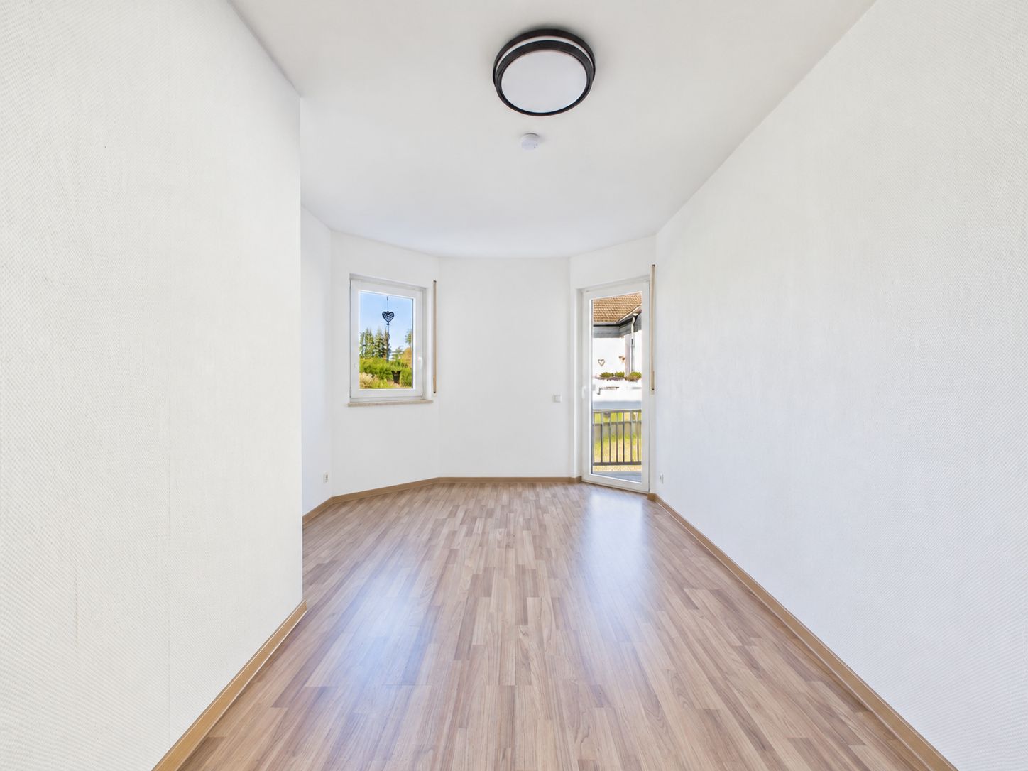 Heller, leerer Raum mit Holzfußboden, zwei Fenstern und weiß gestrichenen Wänden.