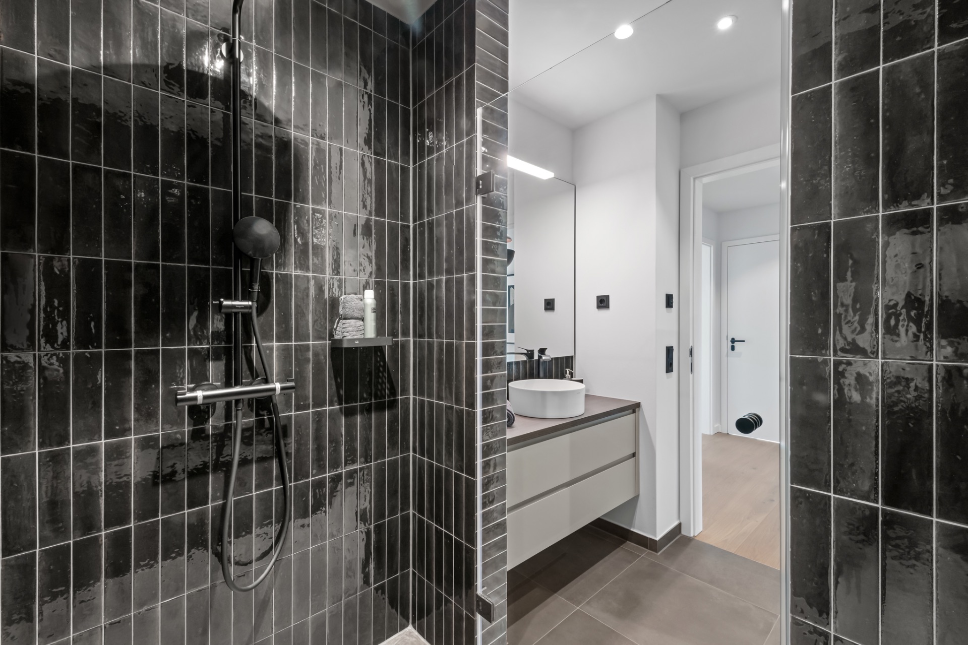 Modernes Badezimmer mit schwarzer Dusche, Waschbecken und großem Spiegel.