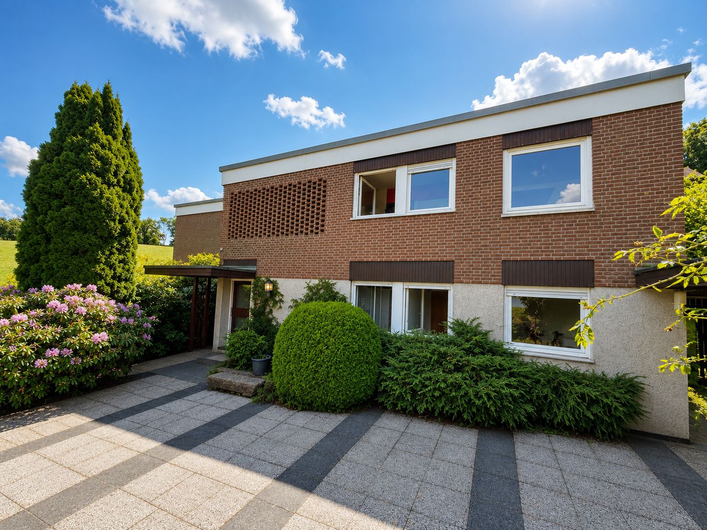 Modernes zweistöckiges Wohnhaus mit Vorgarten, großen Fenstern und gepflastertem Eingangsbereich.