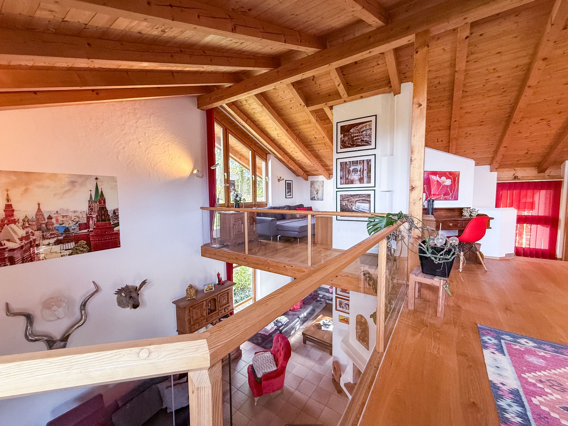 Wohnzimmer mit Galerie, Holzbalkendecke, Glasgeländer und farbenfrohen Möbeln.