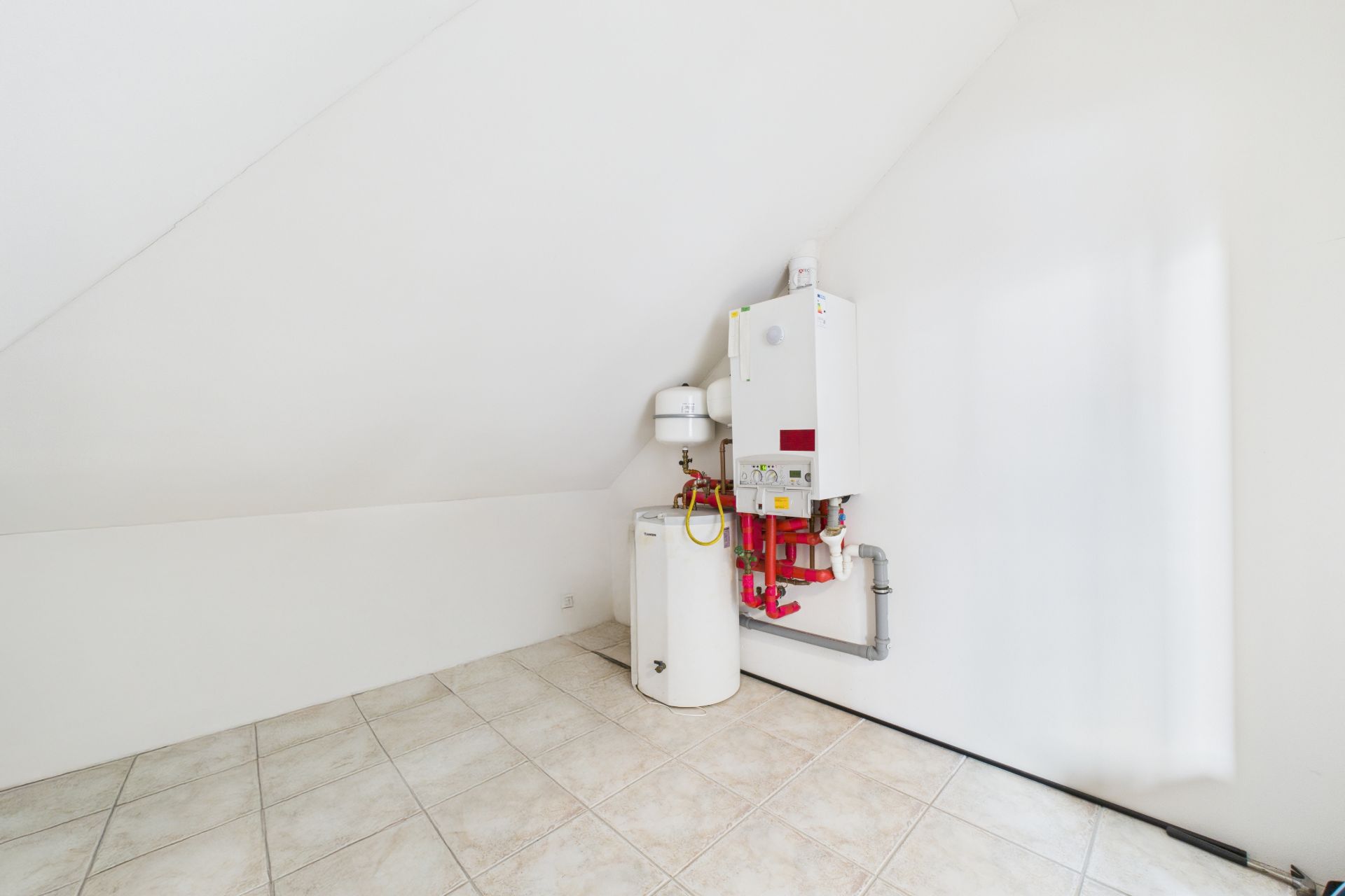 Hauswirtschaftsraum mit einer Heizanlage und einem weißen Boiler auf hell gefliestem Boden.