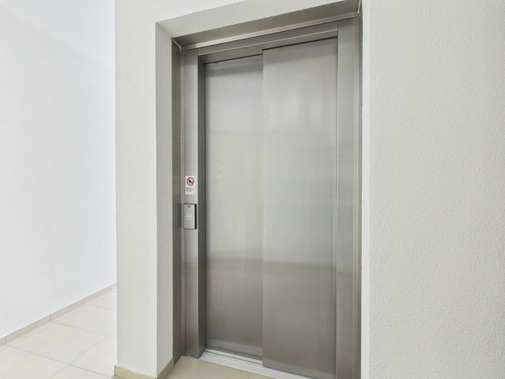 Geschlossener Aufzug mit Edelstahltür in einem hellen Flur.