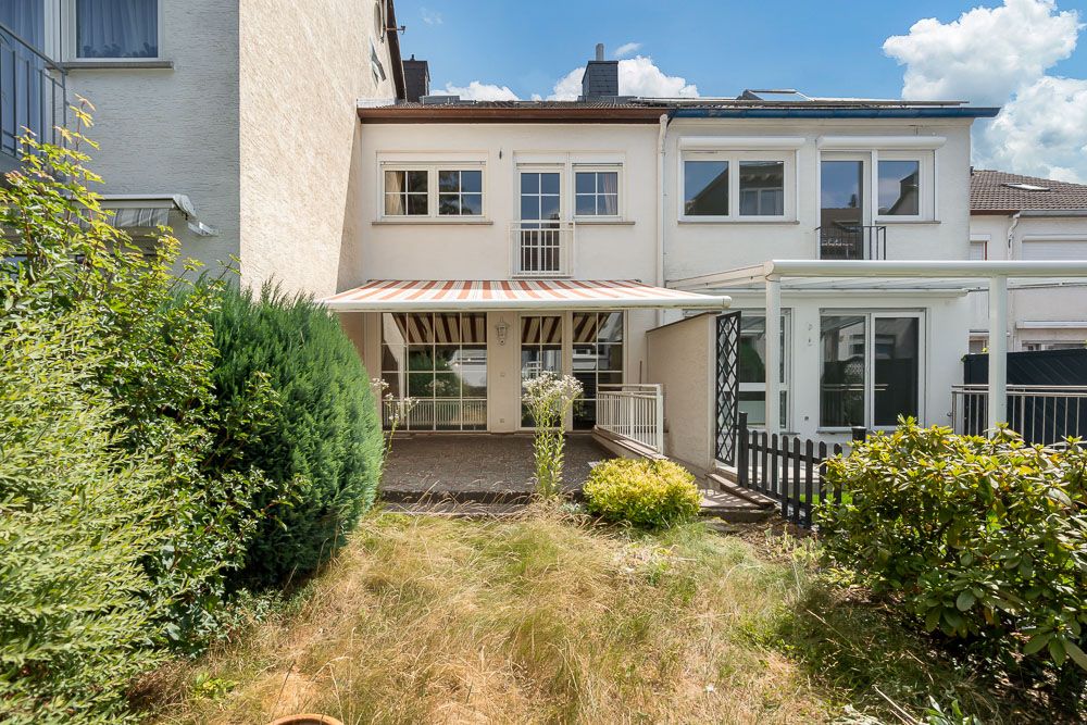 Rückansicht eines Wohnhauses mit Terrasse, Markise und kleinem Garten mit Büschen und Rasen.