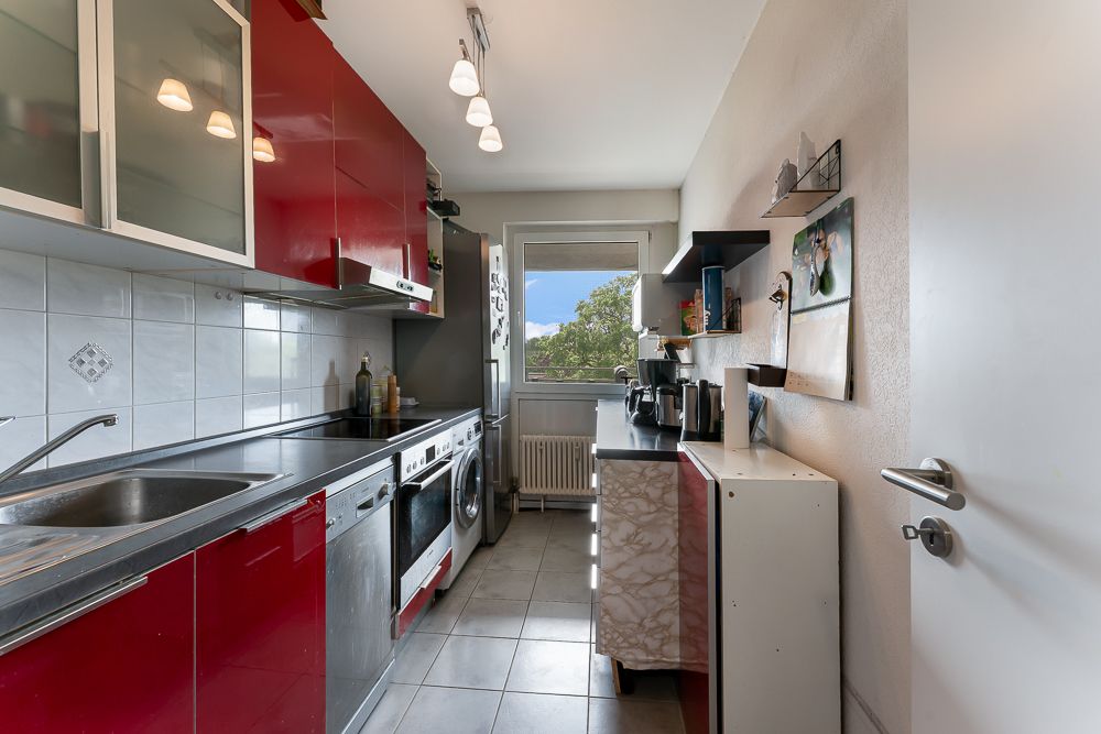 Moderne Küche mit roten Schränken, Geräten und Fenster mit Blick ins Grüne.