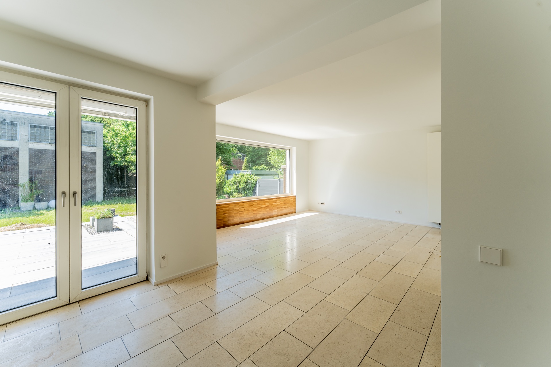 Heller, leerer Raum mit Fliesenboden, großer Fensterfront und Zugang zur Terrasse.