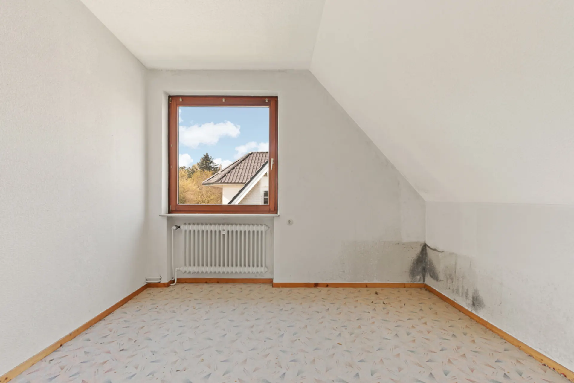 Leeres Zimmer mit Teppich, Fenster, Heizkörper und Schimmel an der rechten Wand.