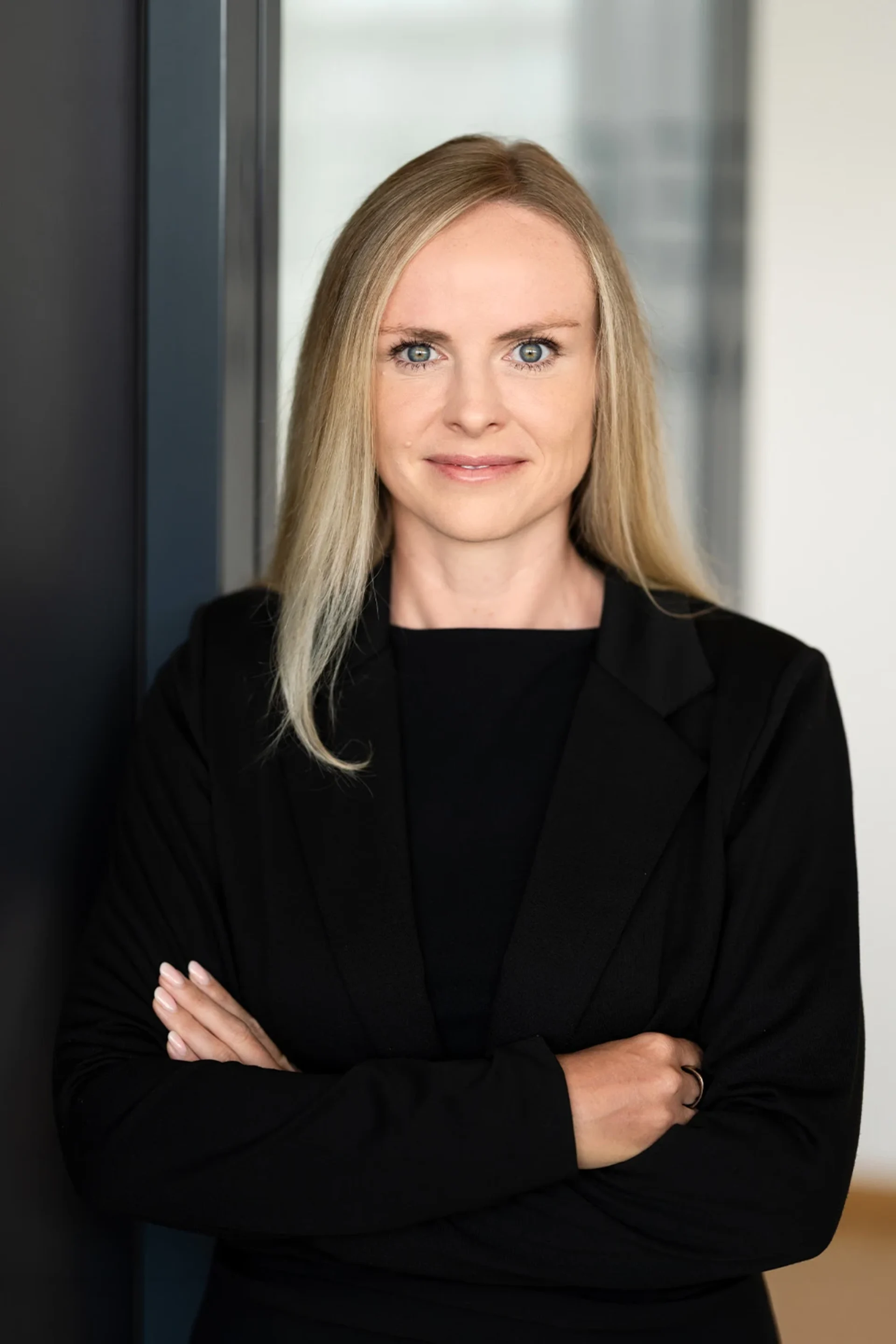 Frau mit langen blonden Haaren und schwarzem Blazer steht mit verschränkten Armen.
