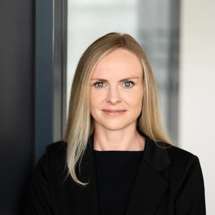 Frau mit langen blonden Haaren und schwarzem Blazer steht mit verschränkten Armen.