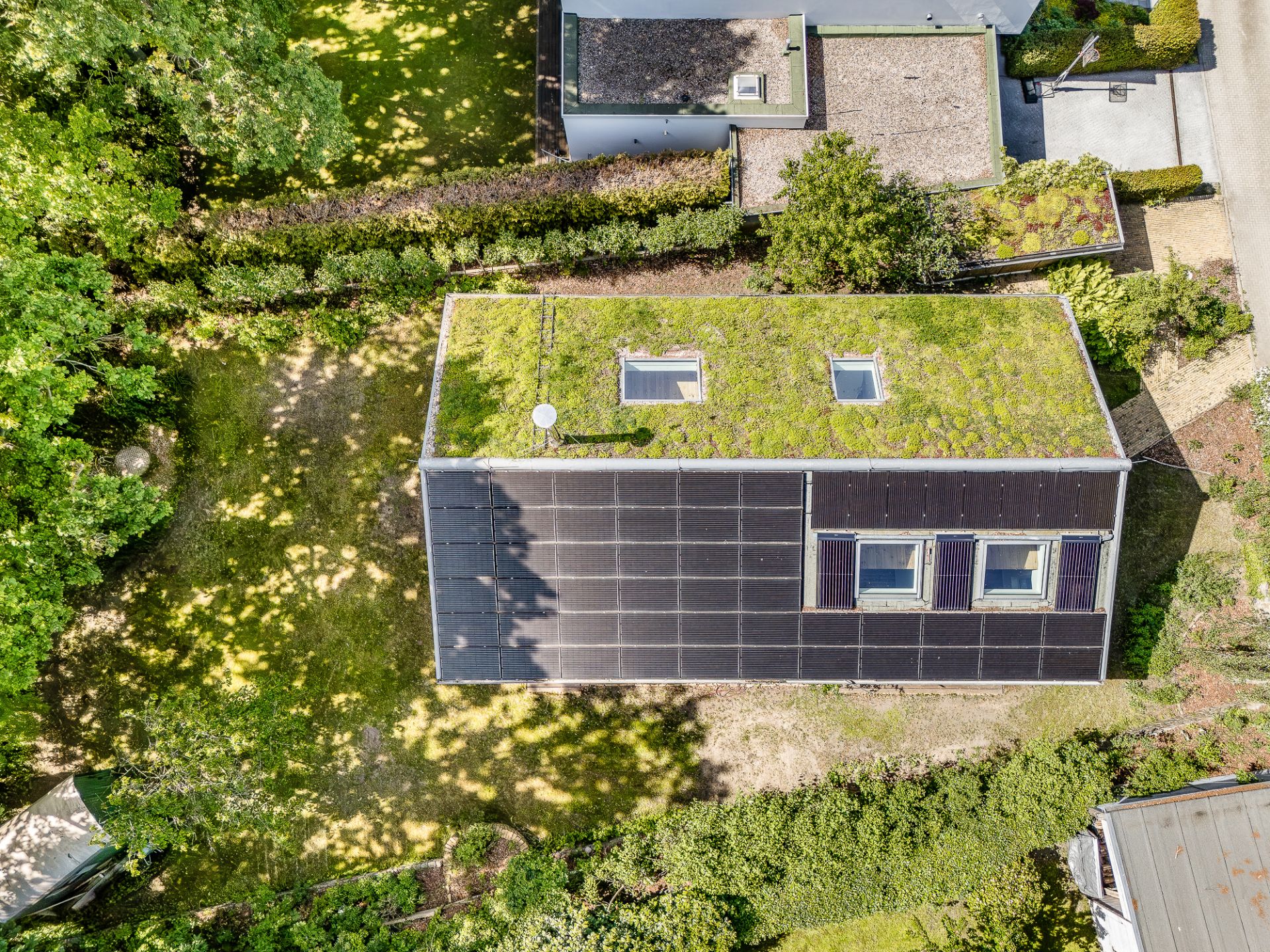 Luftaufnahme eines Hauses mit begrüntem Dach und dunkler Solarfassade im Garten.