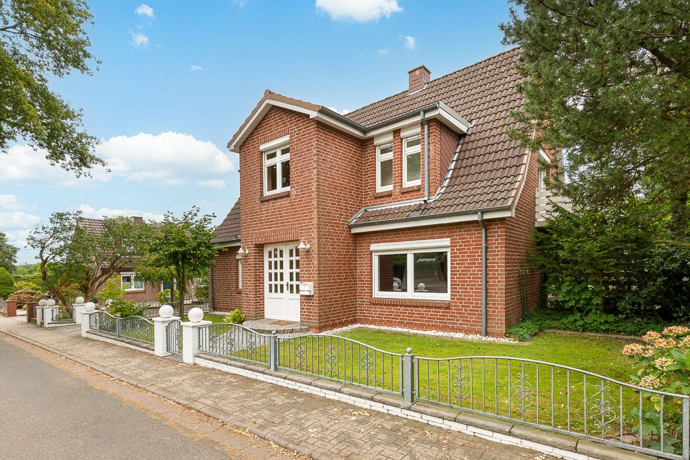 Zweistöckiges Backsteinhaus mit weißer Tür, kleinem Zaun und Garten an einer ruhigen Straße.