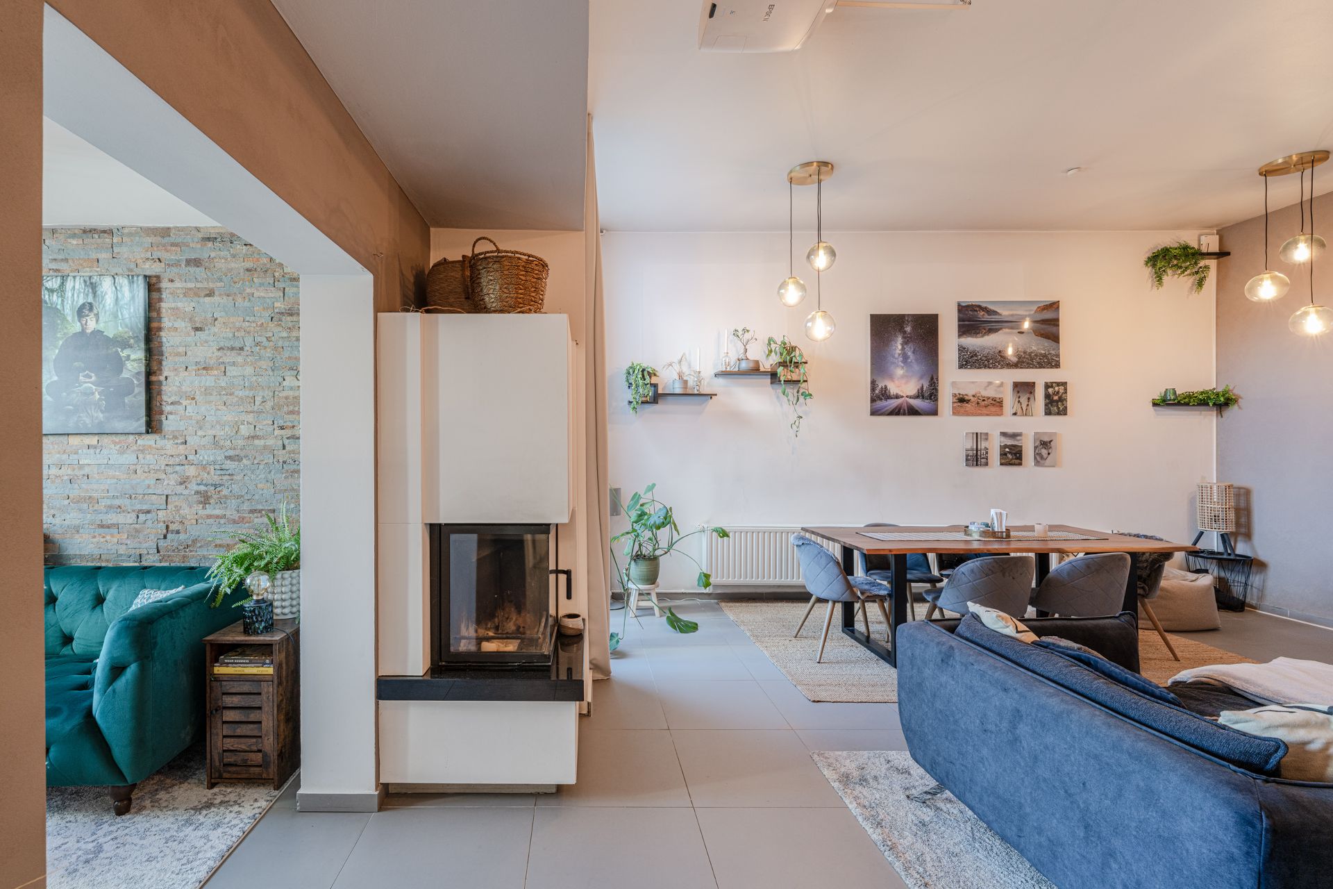 Modernes Wohnzimmer mit Kamin, blauem Sofa, Esstisch und Wandbildern, Pflanzen als Dekoration.