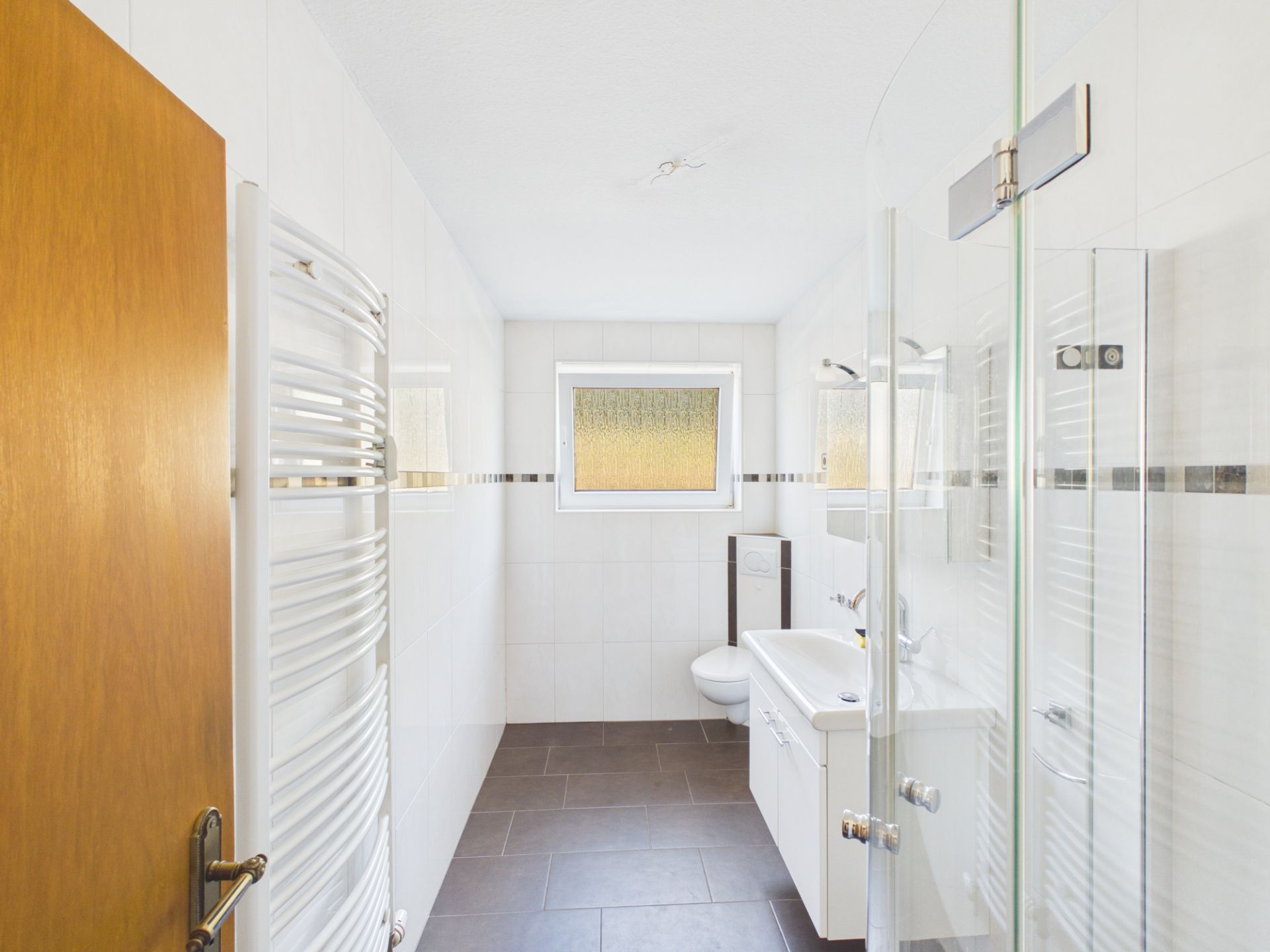 Helles Badezimmer mit Dusche, Waschbecken, Toilette und Fenster.