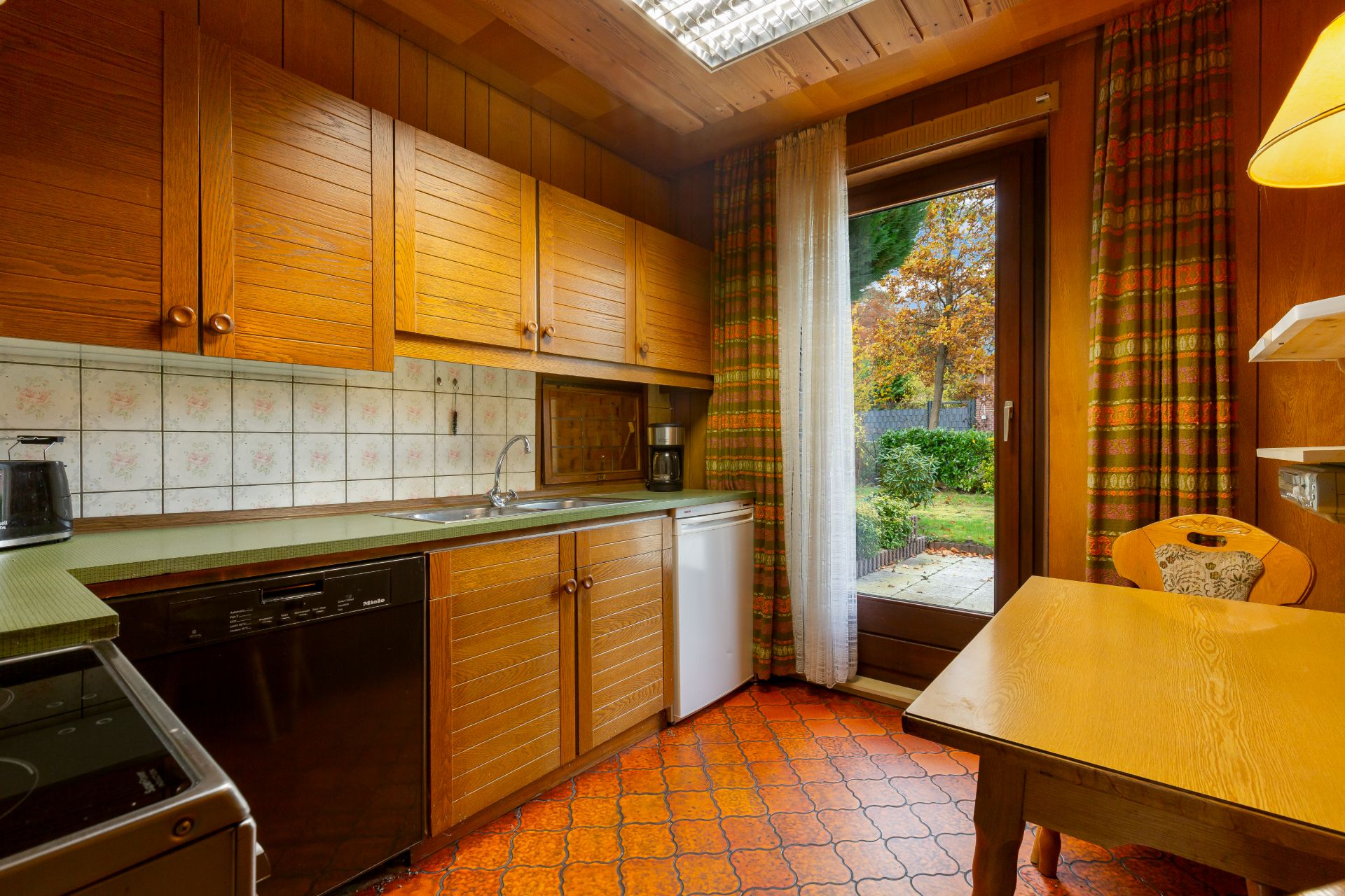 Holzküche mit Tisch, Stühlen, Spülmaschine, Kühlschrank und Zugang zu einem Garten.