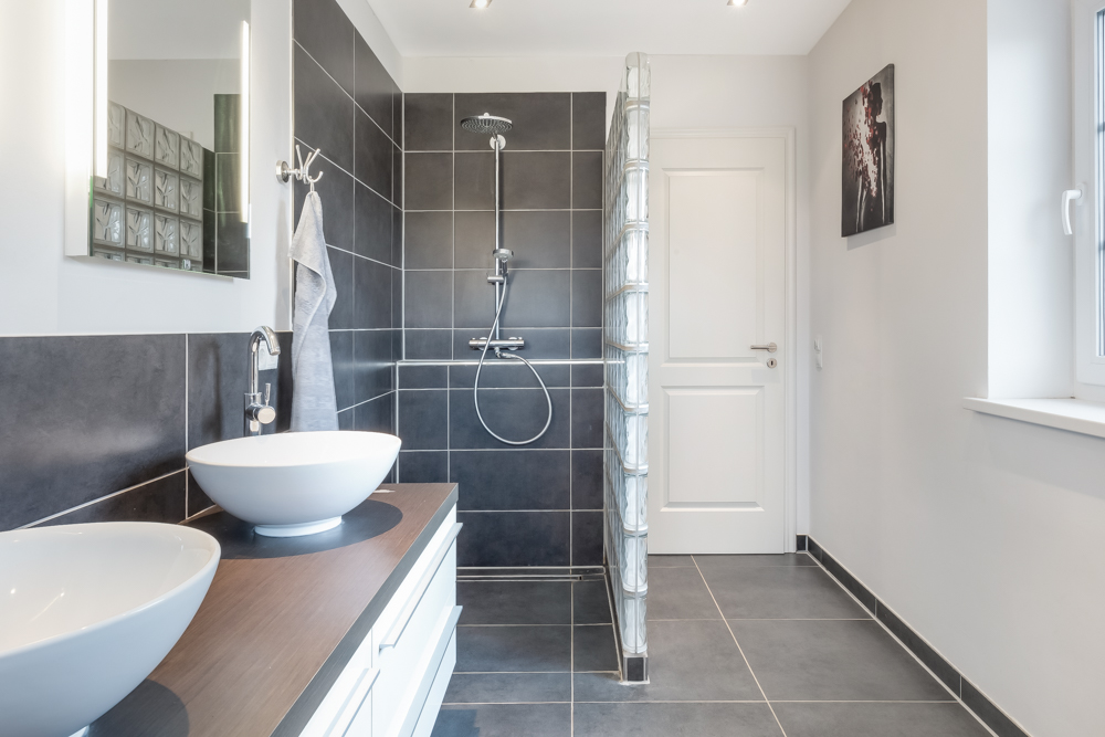 Modernes Badezimmer mit zwei runden Waschbecken, offener Dusche und dunklen Fliesen.