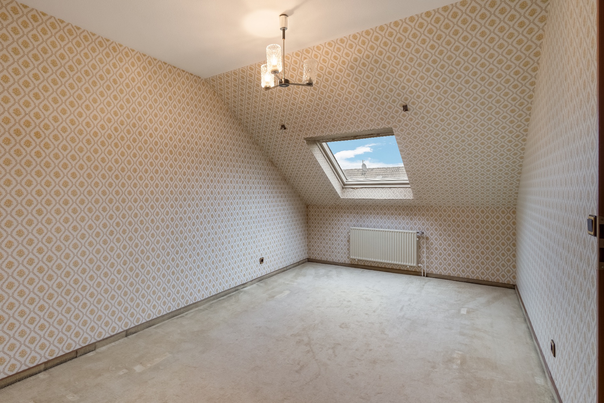 Leeres Zimmer mit gemusterter Tapete, Dachfenster und Heizung unter dem Fenster.