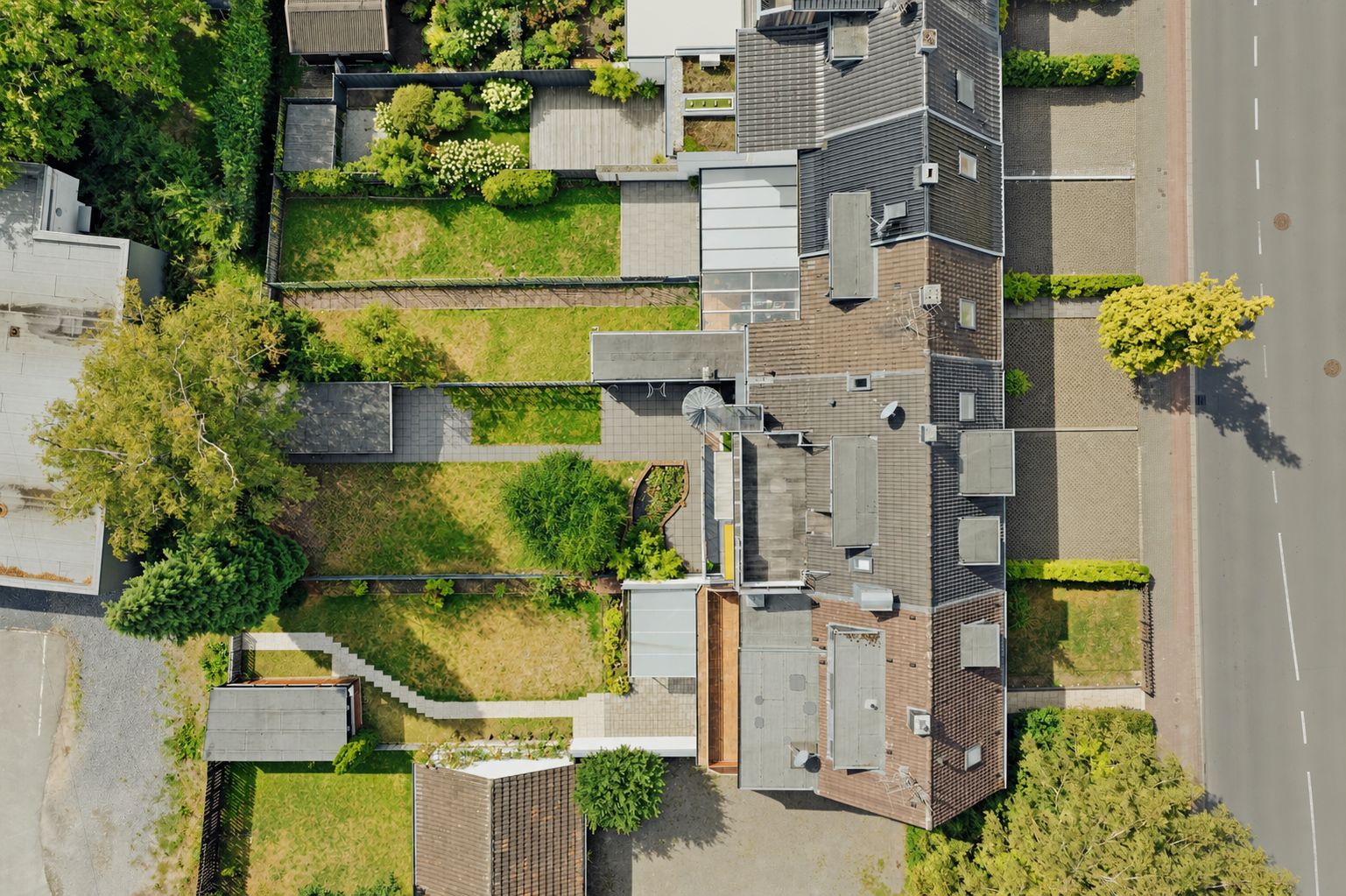 Luftaufnahme eines Wohnhauses mit Gärten, Wegen, Parkplätzen und angrenzender Straße.