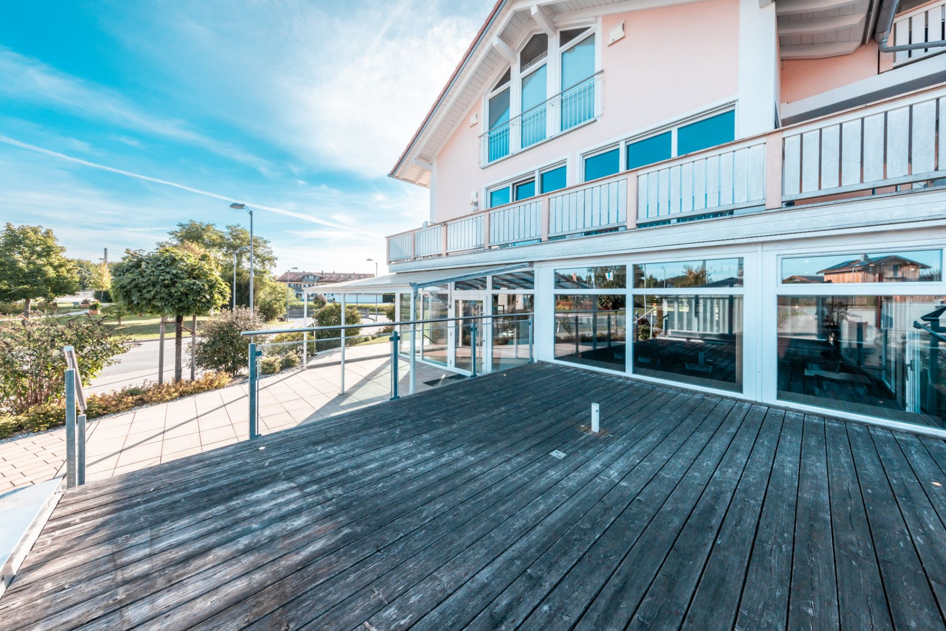 Große Holzterrasse vor einem modernen Wohnhaus mit Glasgeländer und großen Fenstern.