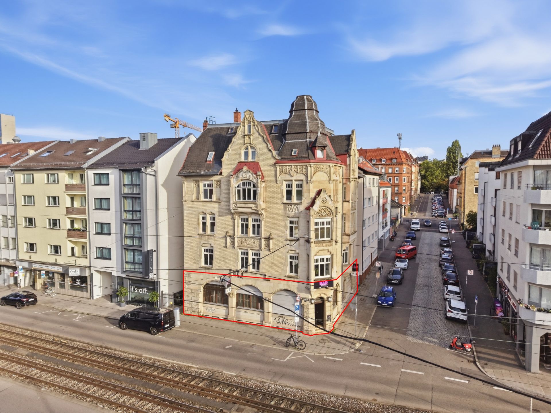 Mehrstöckiges Wohngebäude mit markierter Erdgeschossfläche an einer Straße mit Bahngleisen.