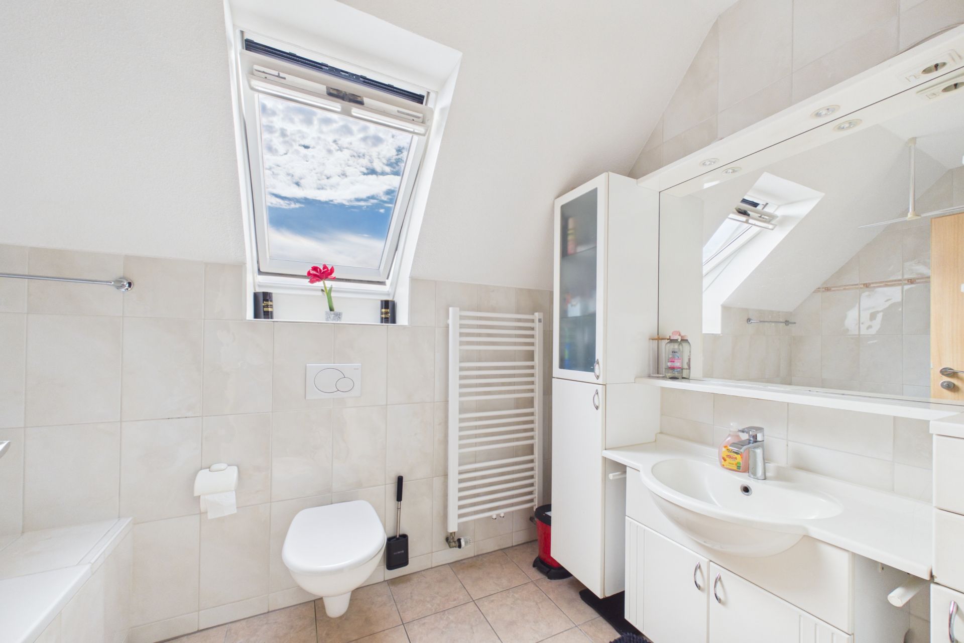 Helles Badezimmer mit Dachfenster, Wandtoilette, Waschbecken und Spiegelschrank.