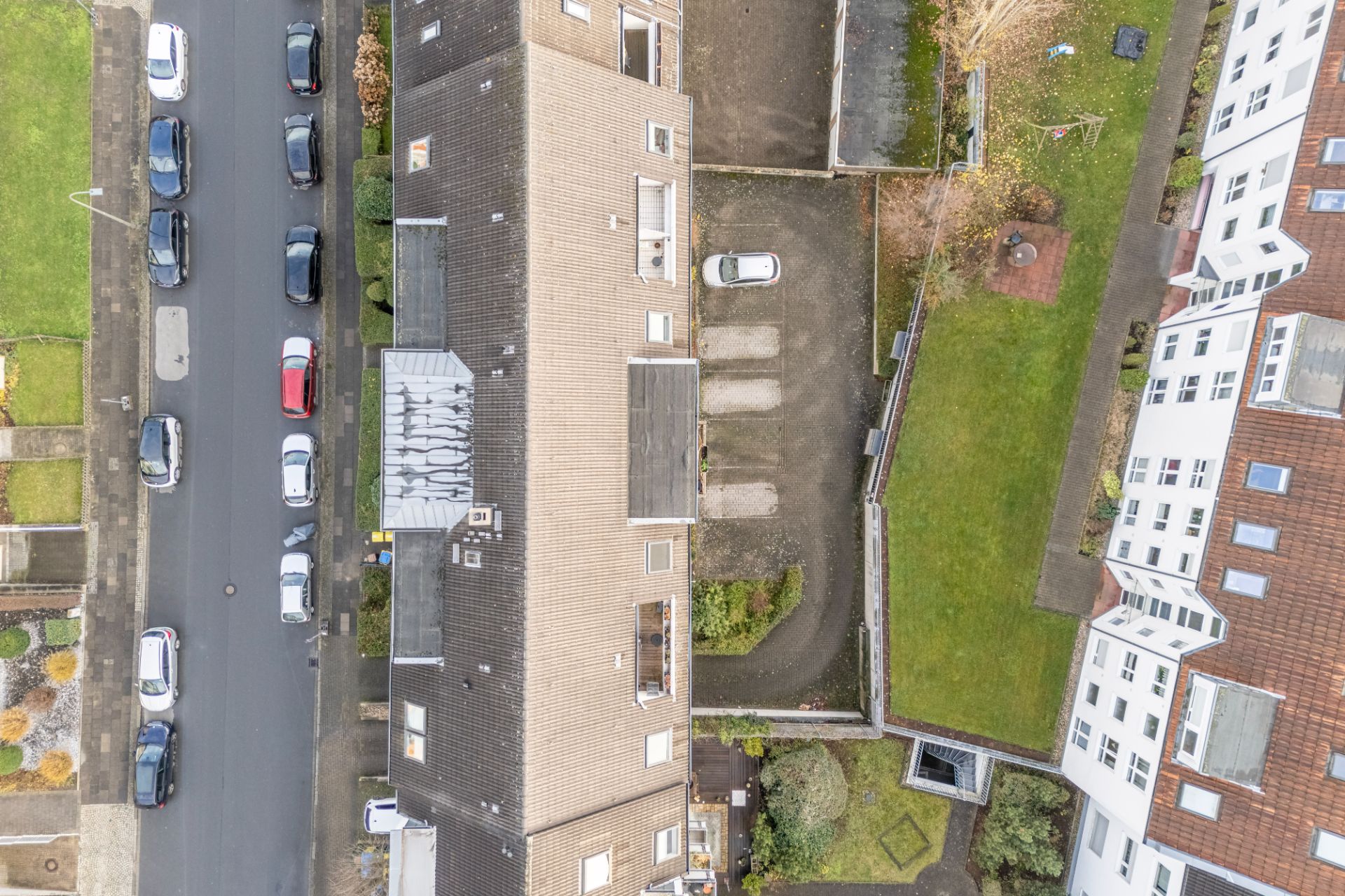 Luftaufnahme eines Wohnhauses mit Parkplatz, Straße und geparkten Autos.
