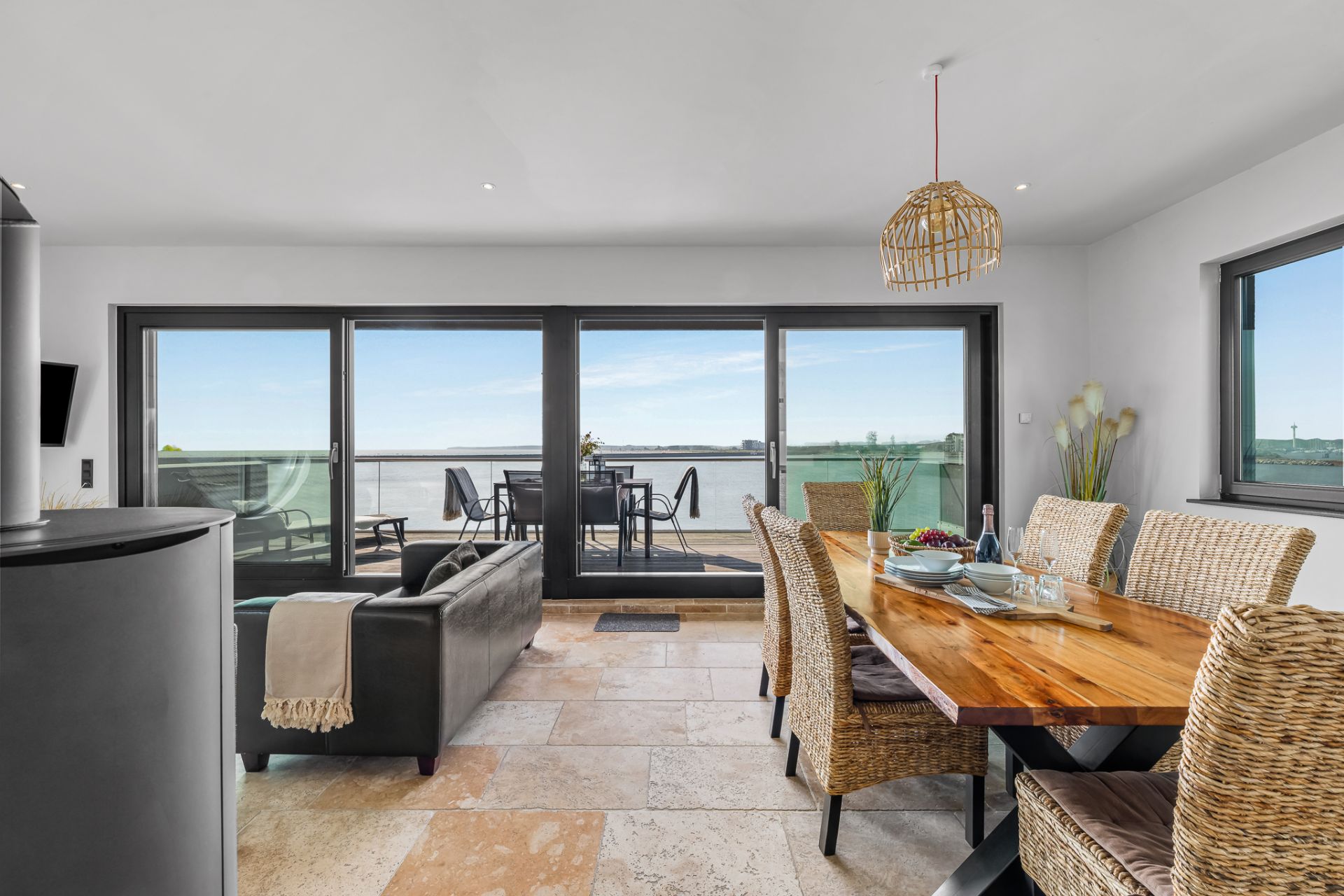 Wohnzimmer mit Essbereich, großem Holztisch und Zugang zu einem Balkon mit Sitzgelegenheit und Seeblick.