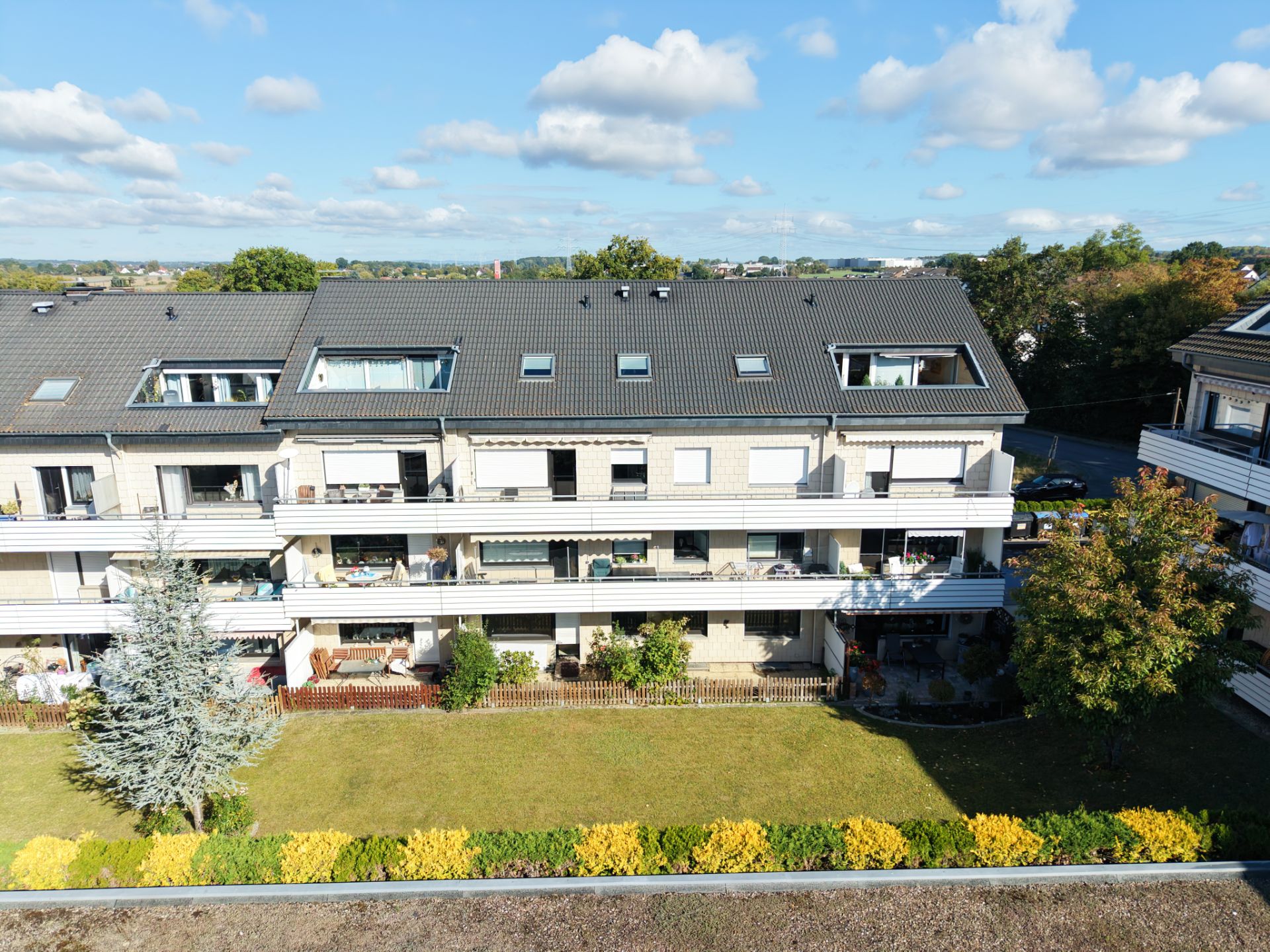 Mehrfamilienhaus mit drei Etagen, Balkonen und Gartenbereich im Vordergrund.