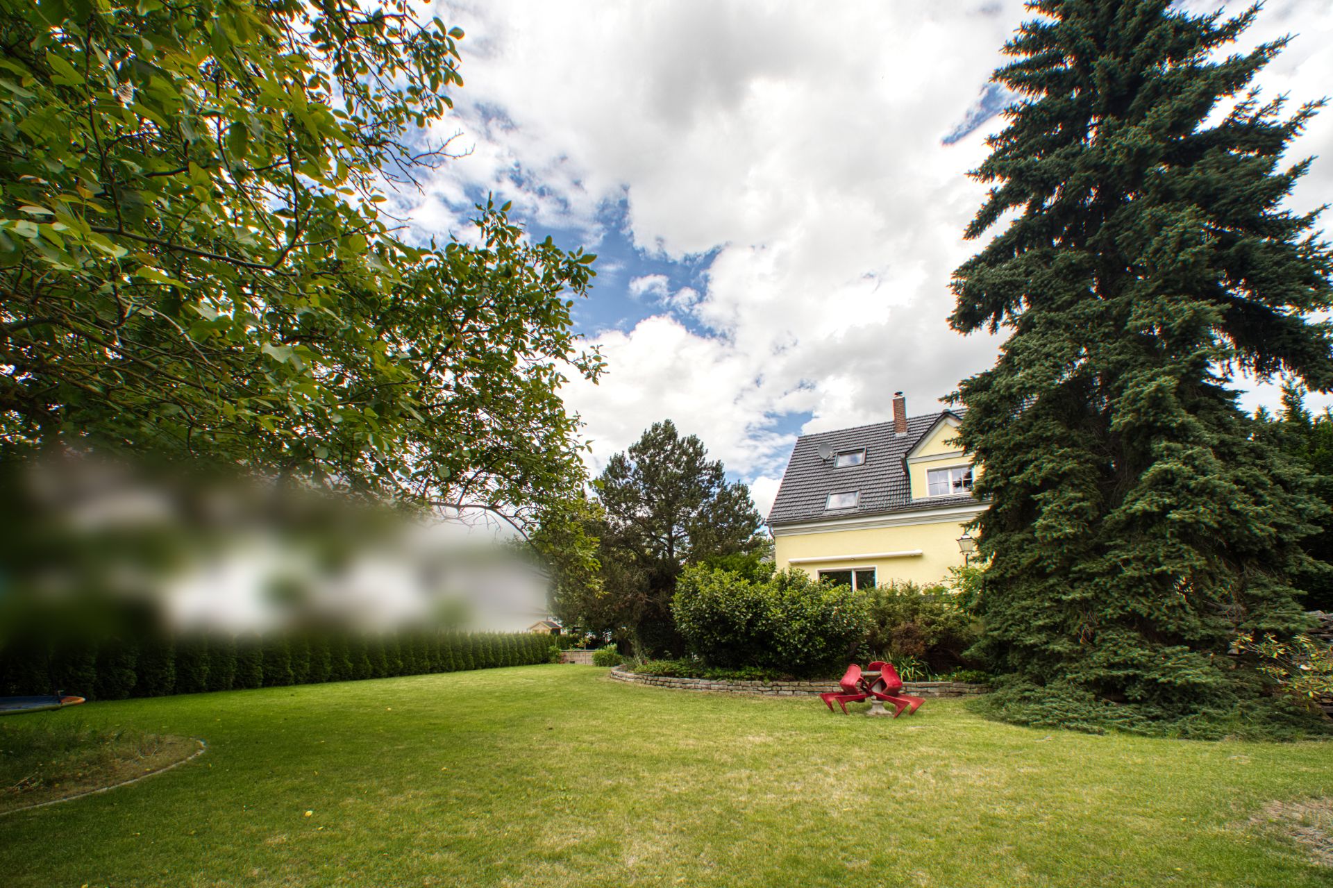 Großer Garten mit Bäumen und Blick auf ein gelbes Wohnhaus im Hintergrund.