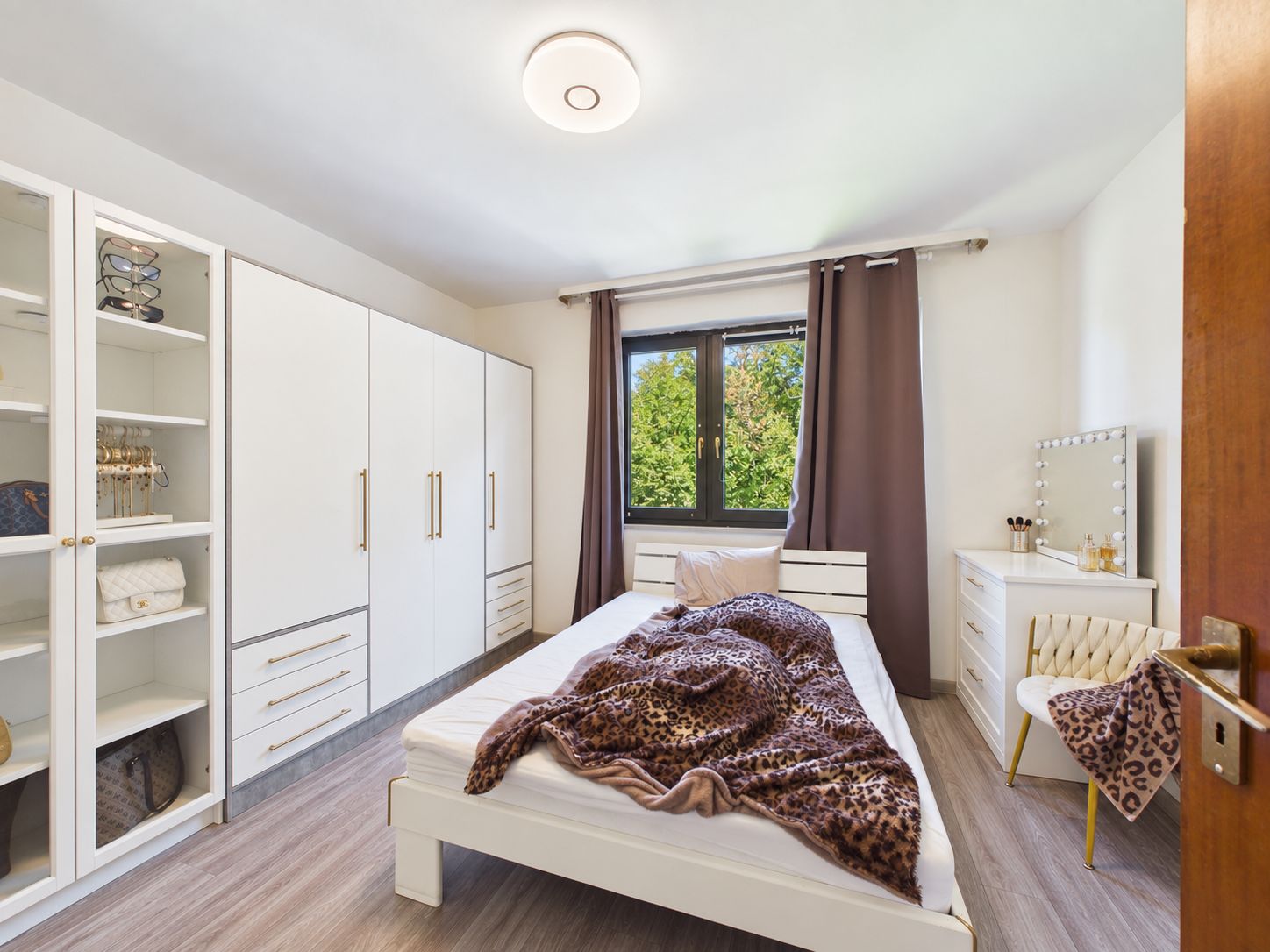 Helles Schlafzimmer mit Bett, Kleiderschränken, Schminktisch und Fenster mit Blick ins Grüne.