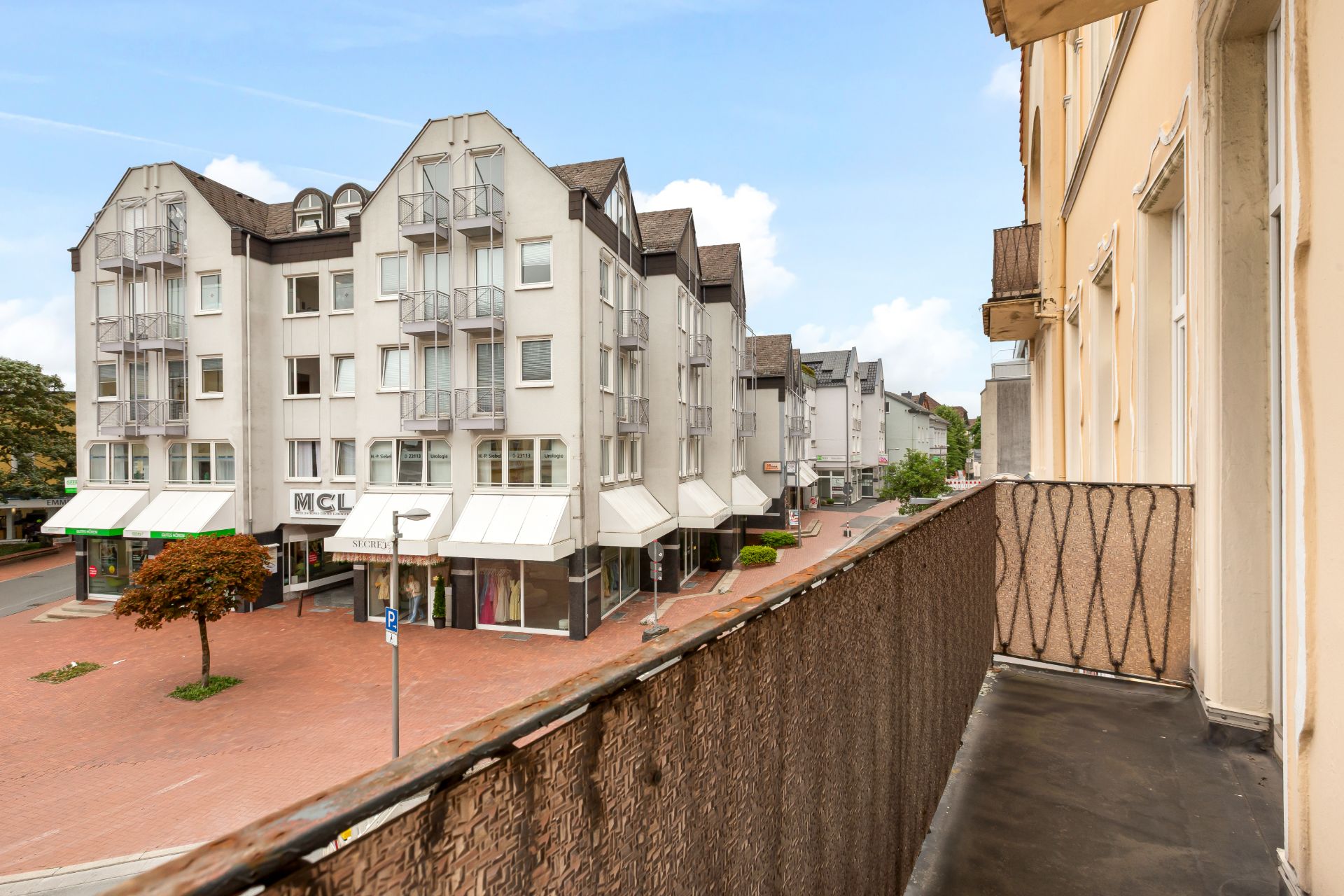 Blick von einem Balkon auf eine ruhige Straße mit modernen Wohngebäuden und Geschäften.