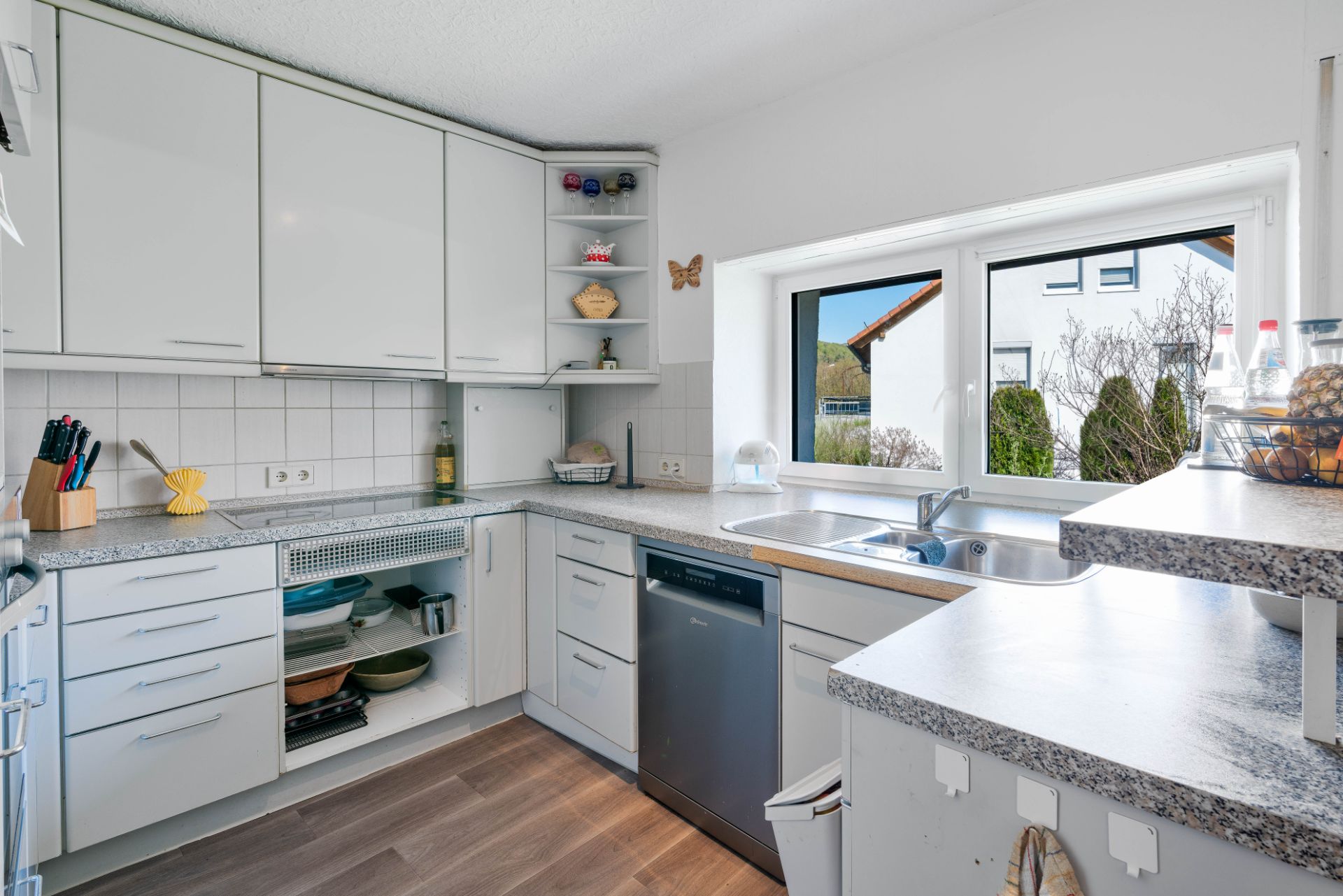 Moderne helle Küche mit weißen Schränken, Spülmaschine, Spüle und großem Fenster.