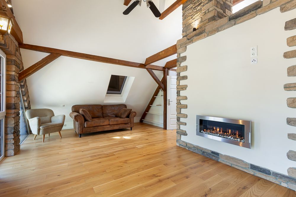 Helles Wohnzimmer mit Holzboden, braunem Sofa, Sessel und modernem Kamin an der Wand.