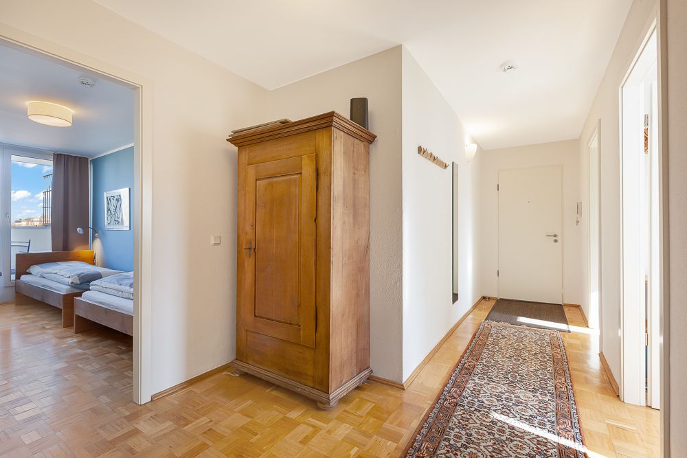 Heller Flur mit Holzschrank, Teppichläufer und Blick in ein Schlafzimmer mit Doppelbett.