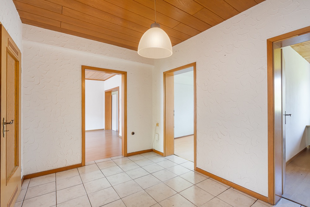 Heller Flur mit Fliesenboden, Holzdecke und mehreren offenen Türen zu angrenzenden Zimmern.